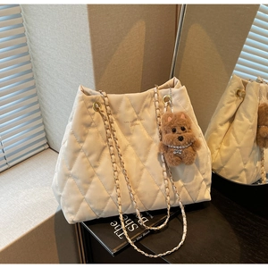 Detail of quilted beige tote bag with gold chain strap and plush puppy charm accessory