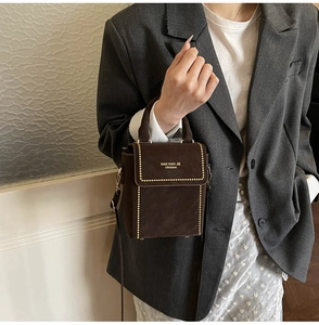 Detail of dark brown suede handbag with gold rivets and logo on flap held by model