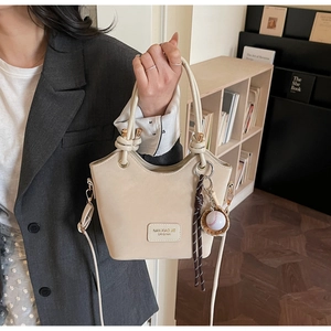 Detail of beige bucket bag featuring branded leather patch and baseball charm