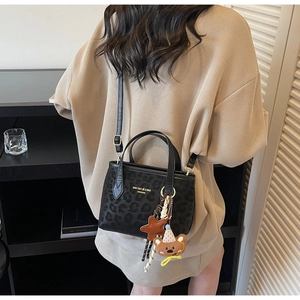 Detail of leopard print tote bag with gold logo and plush bear pendant on model