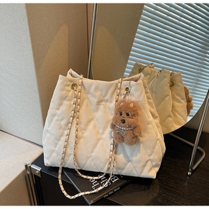 Close-up of beige quilted tote bag with golden chain strap and brown plush puppy charm