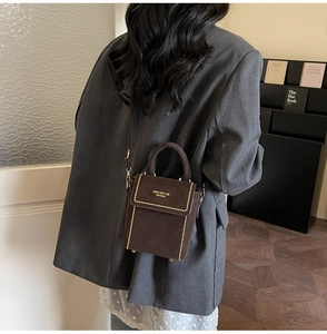 Brown suede crossbody bag featuring gold rivet trim styled with a grey blazer outfit
