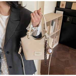 Detail of beige bucket bag featuring a decorative handle knot and baseball charm accessory