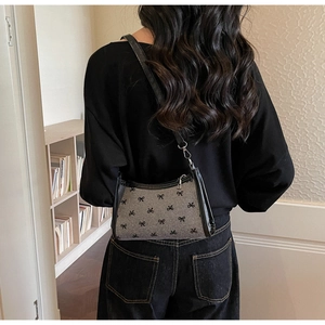 Rear view of a shoulder bag featuring black bow patterns on grey fabric and leather strap
