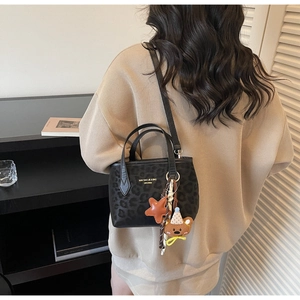 Detail of black leopard print tote bag with bear charm and brand typography design
