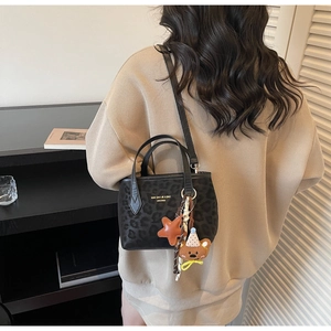Detail of black leopard print tote bag with star and bear charms on long shoulder strap