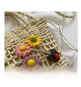 Close-up of handwoven straw bucket bag featuring colorful floral appliques and ladybug charm