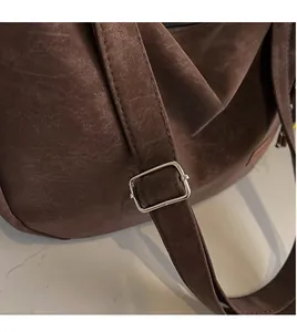 Gros plan de la bandoulière réglable avec boucle argentée sur un sac marron foncé