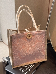 Pink floral embossed tote bag with jute trim and woven rope handles on a book