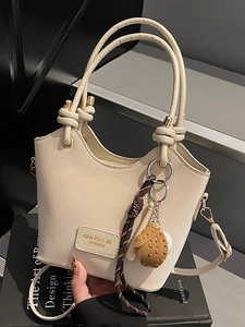 Chic beige bucket bag with decorative knots, shoulder strap and a cute ball charm