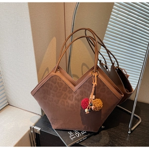 Detail of leopard print suede tote bag with colorful pompom charm in warm lighting