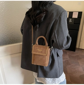 Close-up of small brown crossbody bag with gold rivet accents and brand logo detail