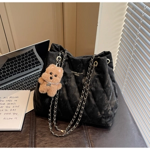 Close-up of black quilted tote bag featuring a gold logo and a brown teddy bear charm