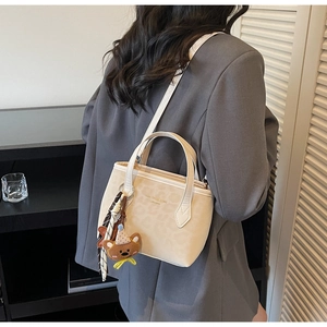 Close-up of beige leopard print tote bag with plush bear charm and striped ribbon detail