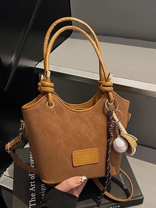 Chic caramel bucket bag with knotted handle and baseball charm on minimalist stairs