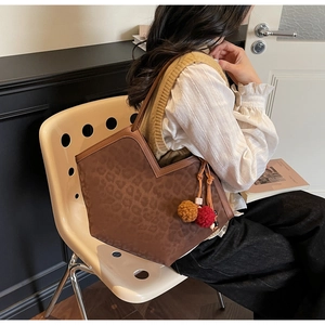 Detail view of large leopard print tote bag with brown leather trim and plush pompom charm