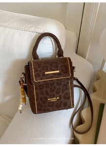 Detail of leopard print crossbody bag with gold rivet trim and beaded charm on white sofa