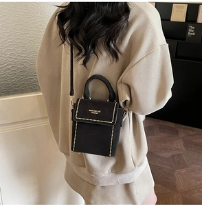 Detail of black suede crossbody bag with gold stud trim and elegant top handle on model