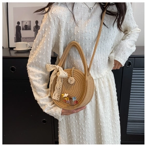 Detail of round straw beach bag featuring lace bow, floral charms, and wood button closure