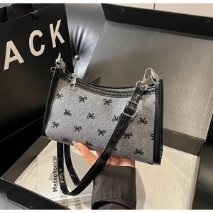 Close-up of gray felt underarm bag with embroidered black bows and leather trim detailing