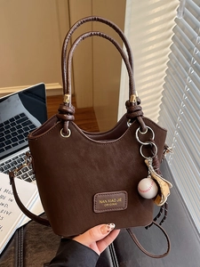 Chic dark brown bucket bag with baseball charm and adjustable strap on a minimalist desk