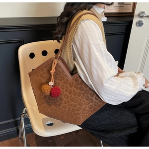 Detail of leopard print tote bag with plush pompom charms shown on a model's shoulder