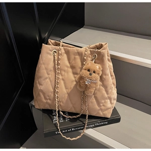 Close-up of quilted apricot tote bag with golden chain strap and brown teddy charm