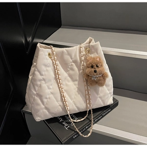 Detail of cream quilted tote bag with gold chain strap and cute brown plush bear charm