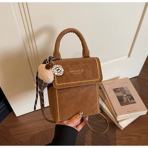 Detail of a brown suede bag with gold studs and a plush ice cream charm decoration