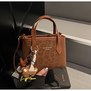 Detail of leopard print brown tote bag with leather trim and hanging bear charm