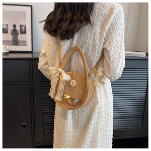 Detail of round straw crossbody bag with white lace bow and animal patches on a model