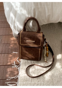Detail of vintage brown leather crossbody bag with gold hardware and beaded charm