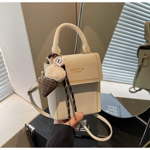Detail of beige square handbag with gold rivet edges and pinecone bag charm accessory