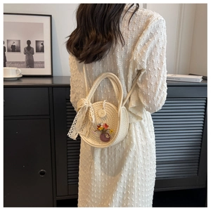 Detail of round straw crossbody bag with lace bow and floral embroidery on a white dress