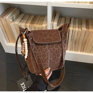 Close-up of brown suede bucket bag with leopard embossed pattern and beaded charm