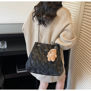 Close-up of black quilted tote bag with chain strap and cute bear plush charm