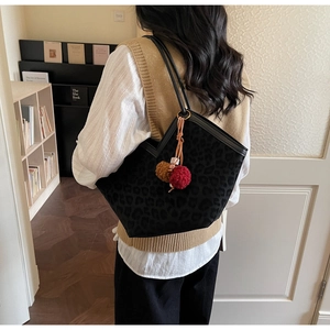 Detail of black leopard print tote bag with plush ball charms on a stylish shoulder strap