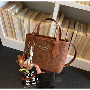 Detail of leopard print tote bag with brown leather handles and a cute plush bear charm