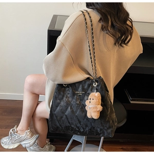 Detail of black quilted tote bag with gold chain strap and cute brown plush bear charm