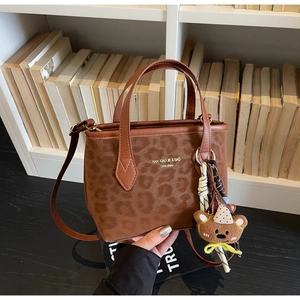 Detail of leopard print tote bag with brown leather handles and cute plush bear charm