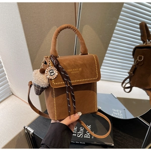 Close-up of brown suede crossbody bag with decorative braided charms and metal hardware