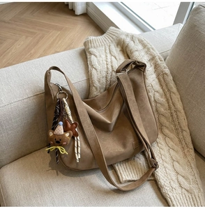 Détail d'un sac bandoulière vintage marron sur canapé avec breloque ours et étoile tricotés