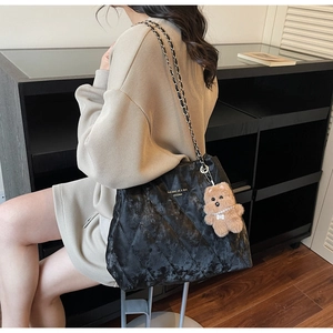 Detail of black quilted tote bag with chain strap and cute plush bear charm accessory