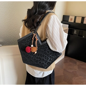 Detail of leopard print tote bag with plush pompom charm shown on shoulder in cozy setting