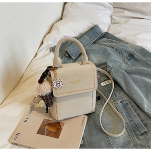 Chic cream leather handbag with gold rivets and cute ice cream charm on a cozy bedding setup