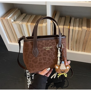 Detail of leopard print tote bag with brown leather handles and a cute bear charm