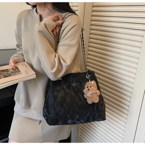 Detail of black quilted tote bag with chain strap and cute brown teddy bear charm