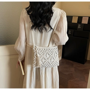 Detail of a beige woven crossbody bag featuring tassels and textured bohemian patterns