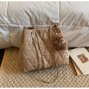 Close-up of quilted khaki tote bag with gold chain strap and plush bear charm