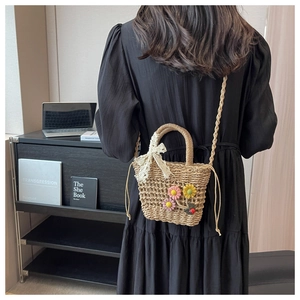 Close-up of handwoven straw bucket bag with floral accents on a black dress backdrop